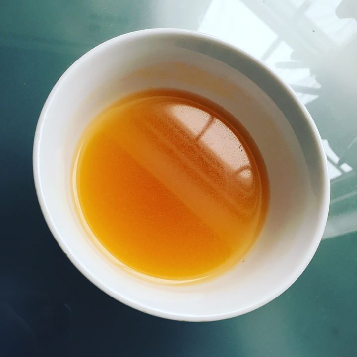 Refreshing sea buckthorn juice blended with sea buckthorn and cinnamon tea in a small tea cup with blue glass background.