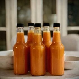 Bottles of Seaberry Hot Sauce sitting on a marble table with a glass and white wood cabinet in the background