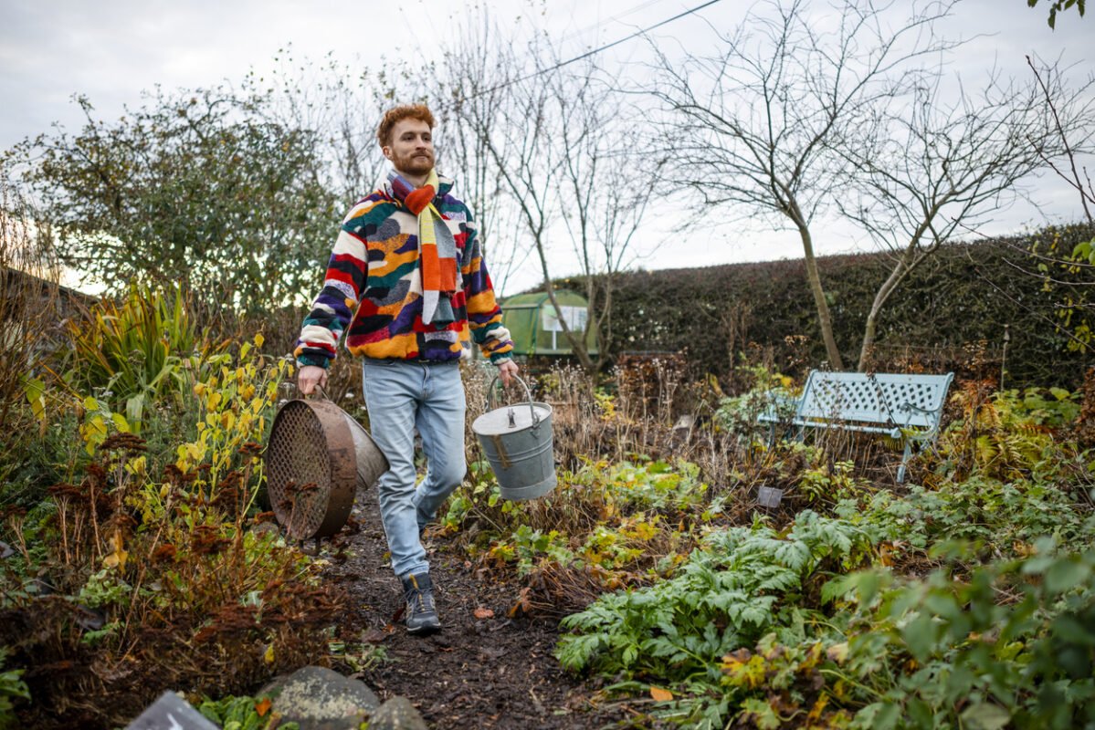 Man walking in a garden carrying tools going to work on the Permaculture Farmstead.