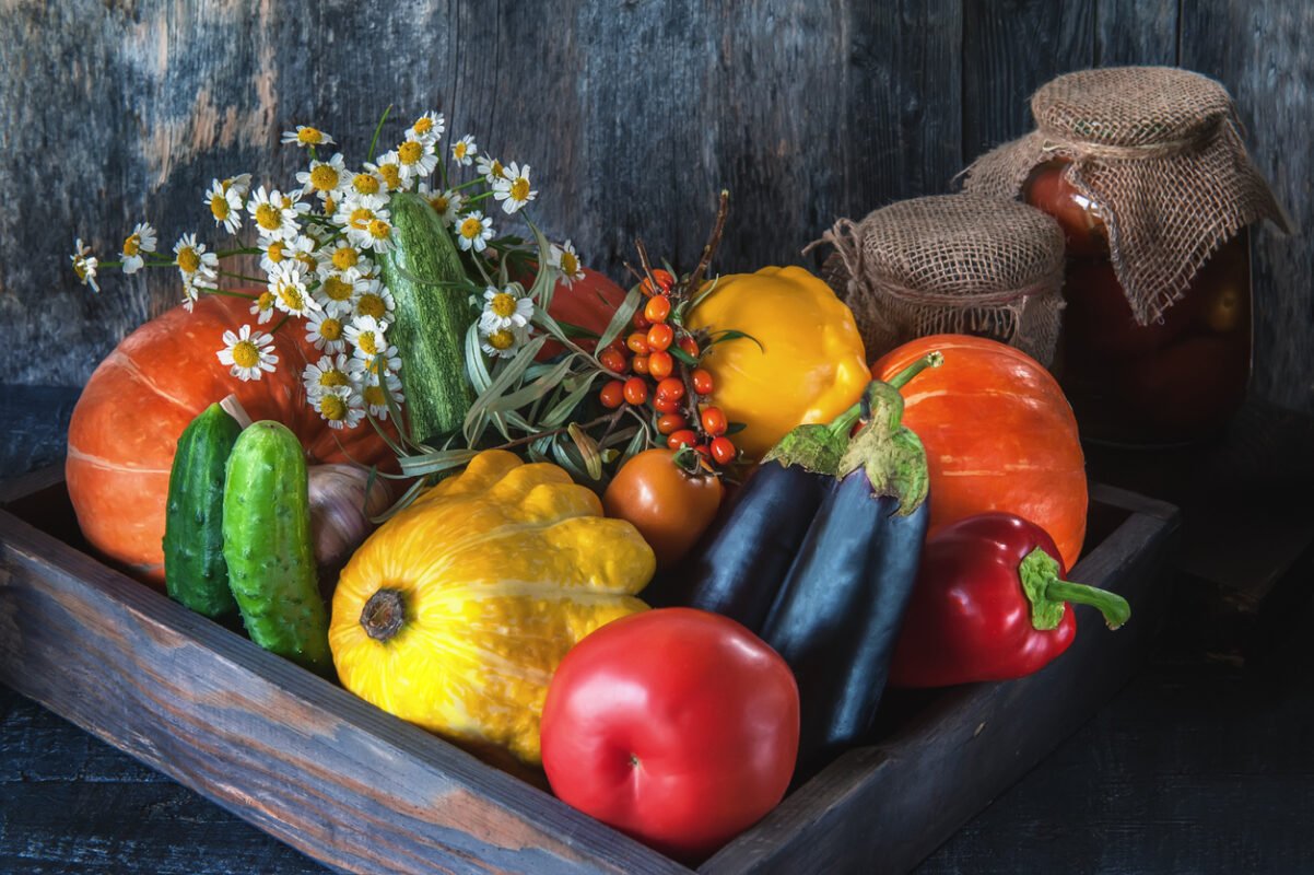 Assorted vegetables, pumpkin, zucchini, eggplant, garlic, green onions, and tomatoes with sea buckthorn berries on a wooden background in rustic style with flowers daisies for Thanksgiving.