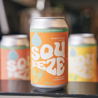 A Can of Squeeze Seabuckthorn + Ginger Sparkling Water, made by Booch in front of two of Booch sparkling water flavours obscured in the background.