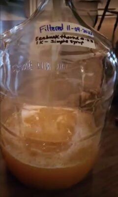 Sea berry cider pouring into a glass fermentation jug.